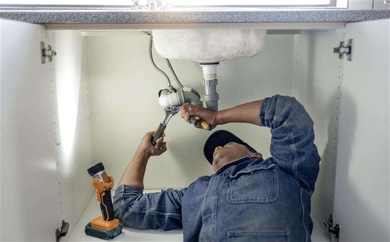 Plumber repairing pipes beneath a bathroom sink in Delray Beach