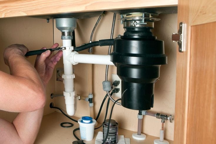 Plumber installing a garbage disposal beneath a kitchen sink in Delray Beach