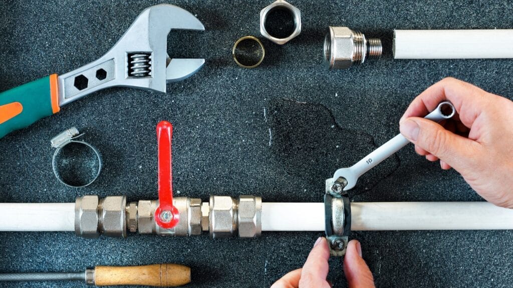 Plumber repairing a pipe valve with an adjustable wrench in Delray Beach