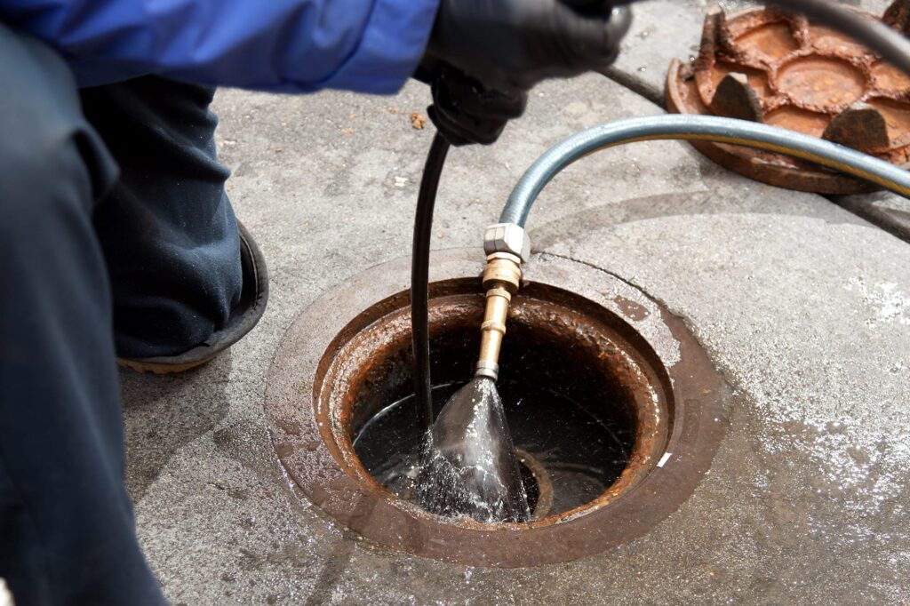 Plumber hydro jetting a sewer line through a manhole in Delray Beach