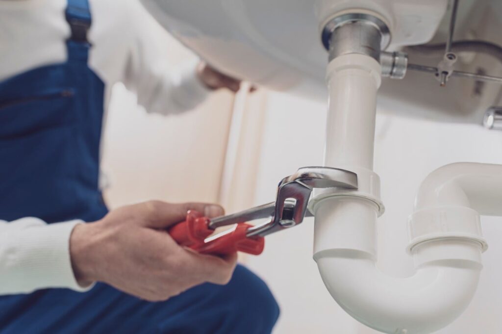 Plumber repairing a white drain pipe beneath a sink in Delray Beach
