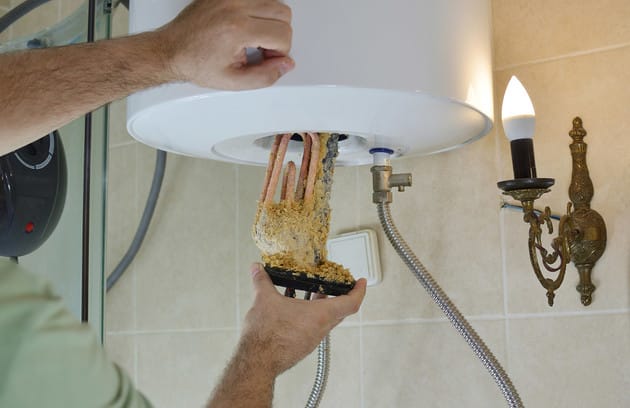 Technician removing mineral buildup from a water heater in Delray Beach